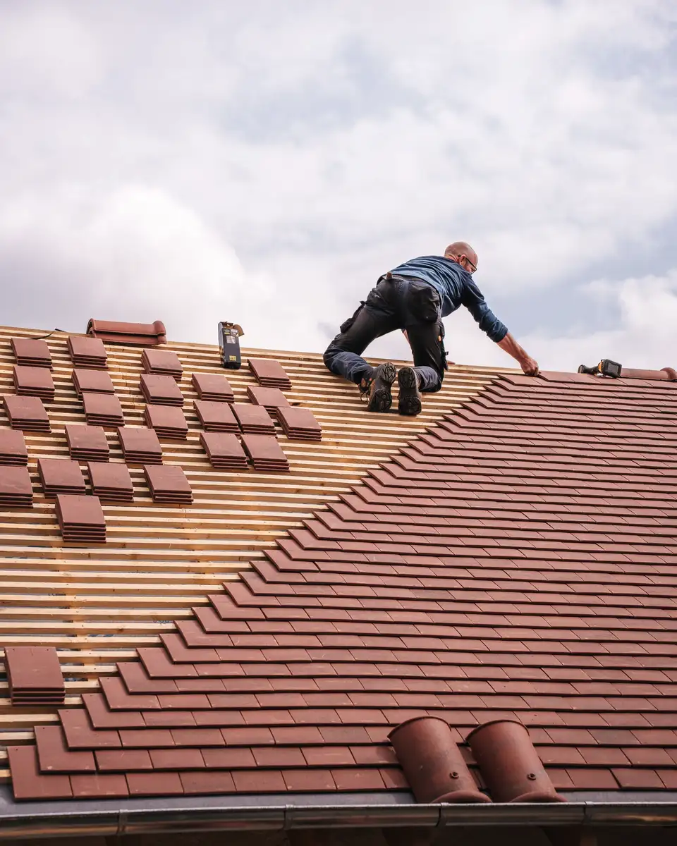 Roofer working on a pitched tile roof under a grey sky